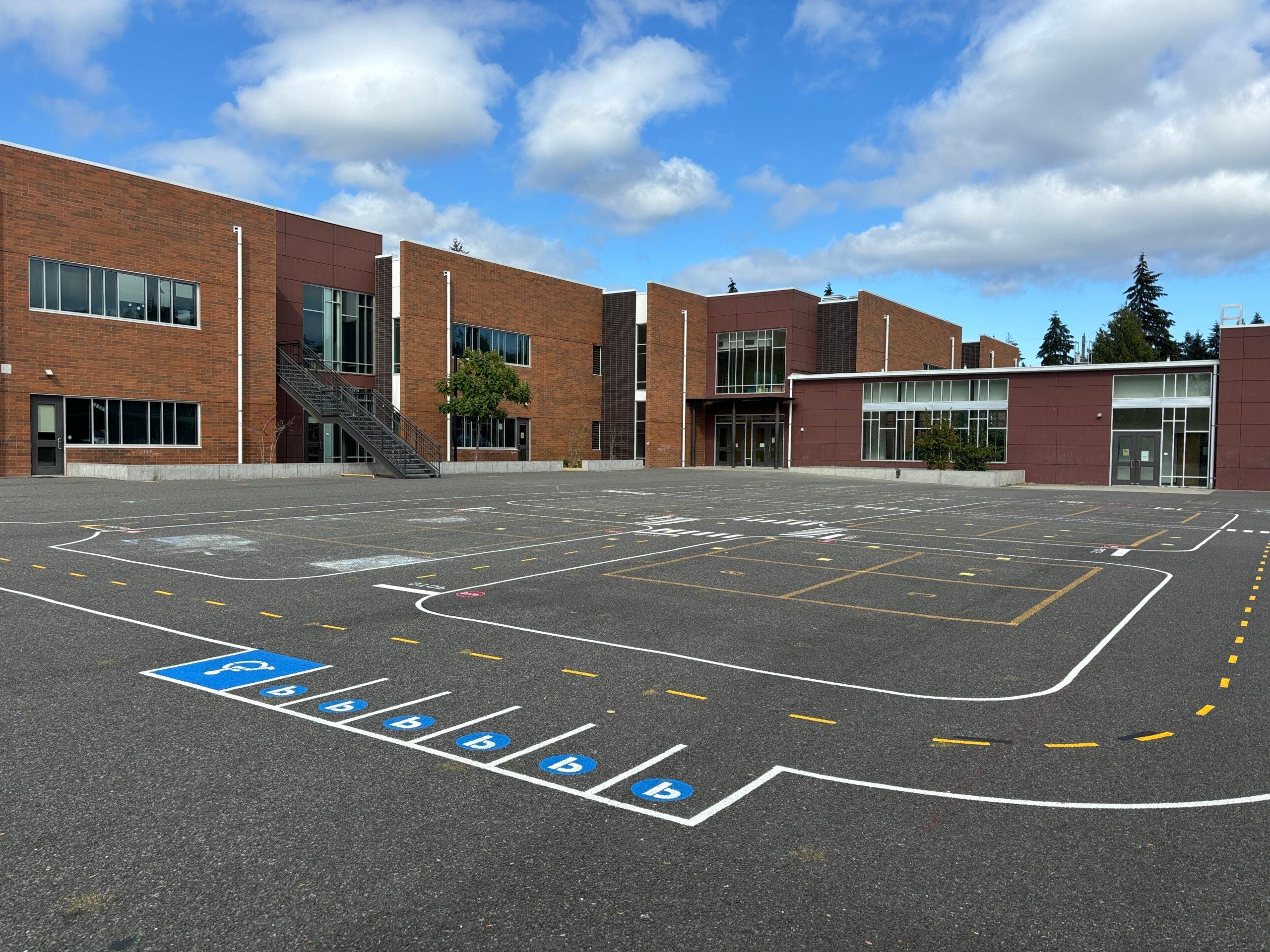 Miniature road with parking stalls painted on blacktop with school in background.